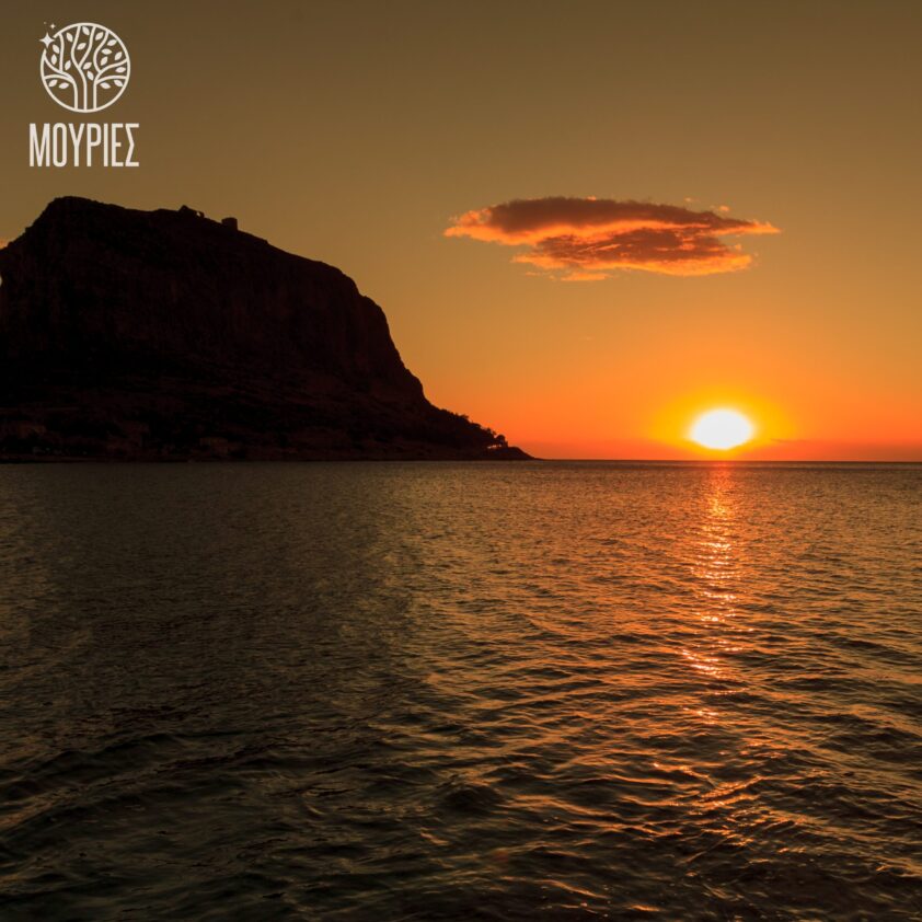 Monemvasia Castle silhouetted against a golden sunset over the sea