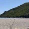 Untouched Mediterranean beach beneath an emerald hillside