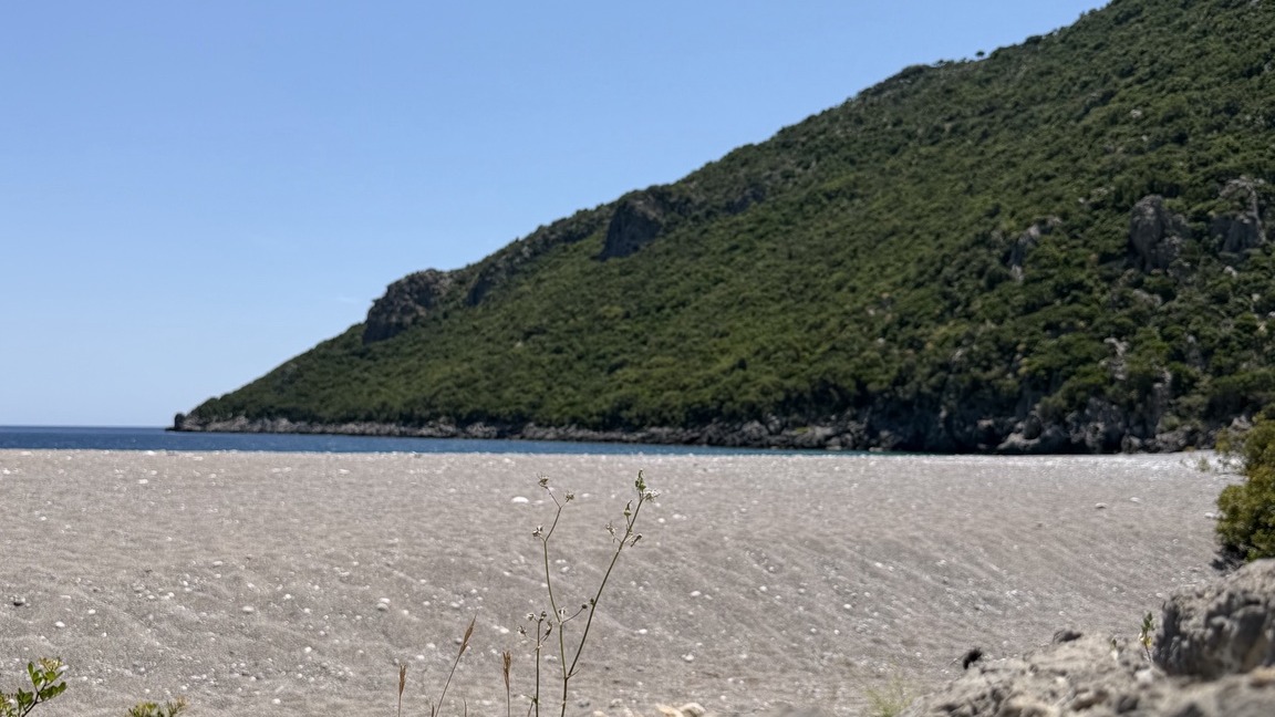 Untouched Mediterranean beach beneath an emerald hillside